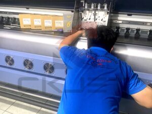 Kỹ thuật viên đang kiểm tra máy in bạt khổ lớn theo hướng dẫn sử dụng để đảm bảo chất lượng in ấn