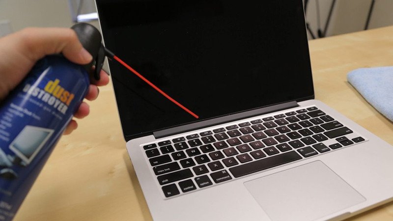 Người dùng đang dùng bình khí nén để thổi bụi bàn phím khi vệ sinh máy tính laptop